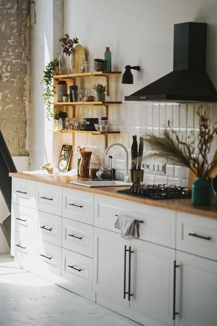 about-us-01 Sunlit modern kitchen in Scandinavian style with wooden shelves and white cabinetry.