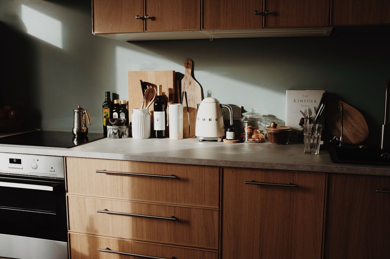 A stylish kitchen with wooden cabinets and modern accessories lit by morning sunlight.