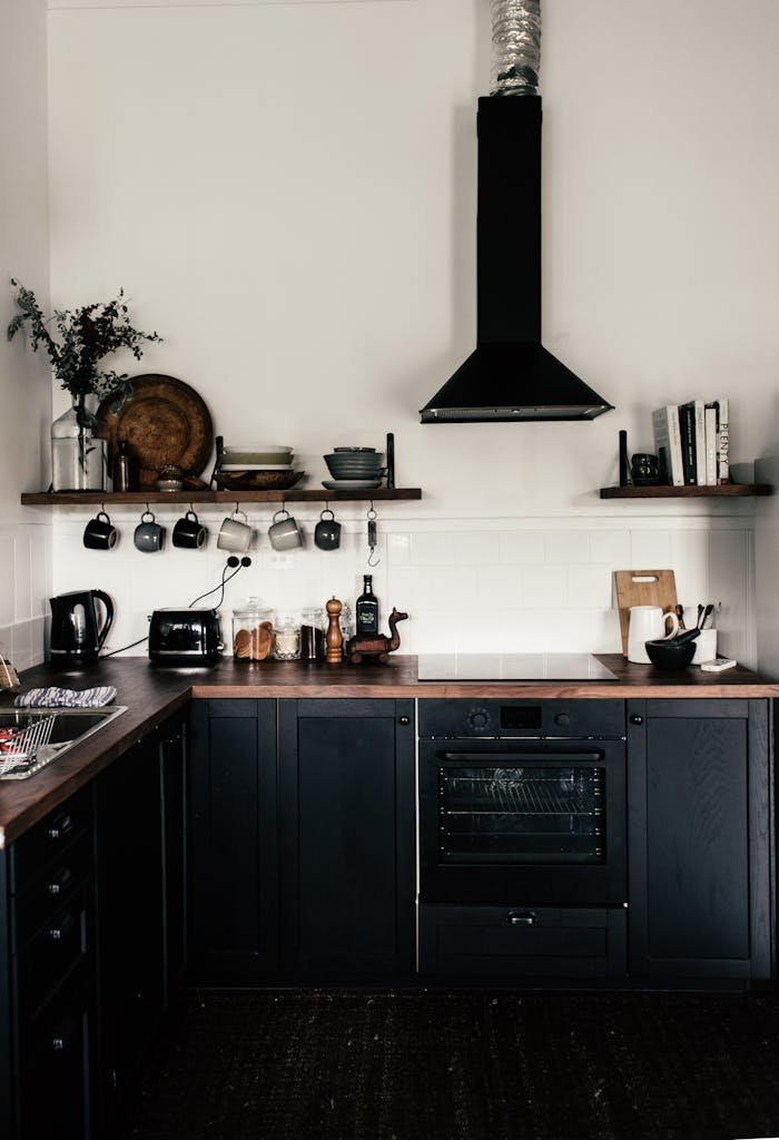 about-us-02 Interior of contemporary kitchen with black wooden cupboards and shelves with various utensils and appliances
